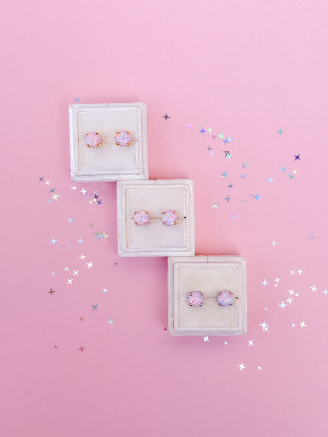 3 pairs of pink opal stud earrings on a pink background.