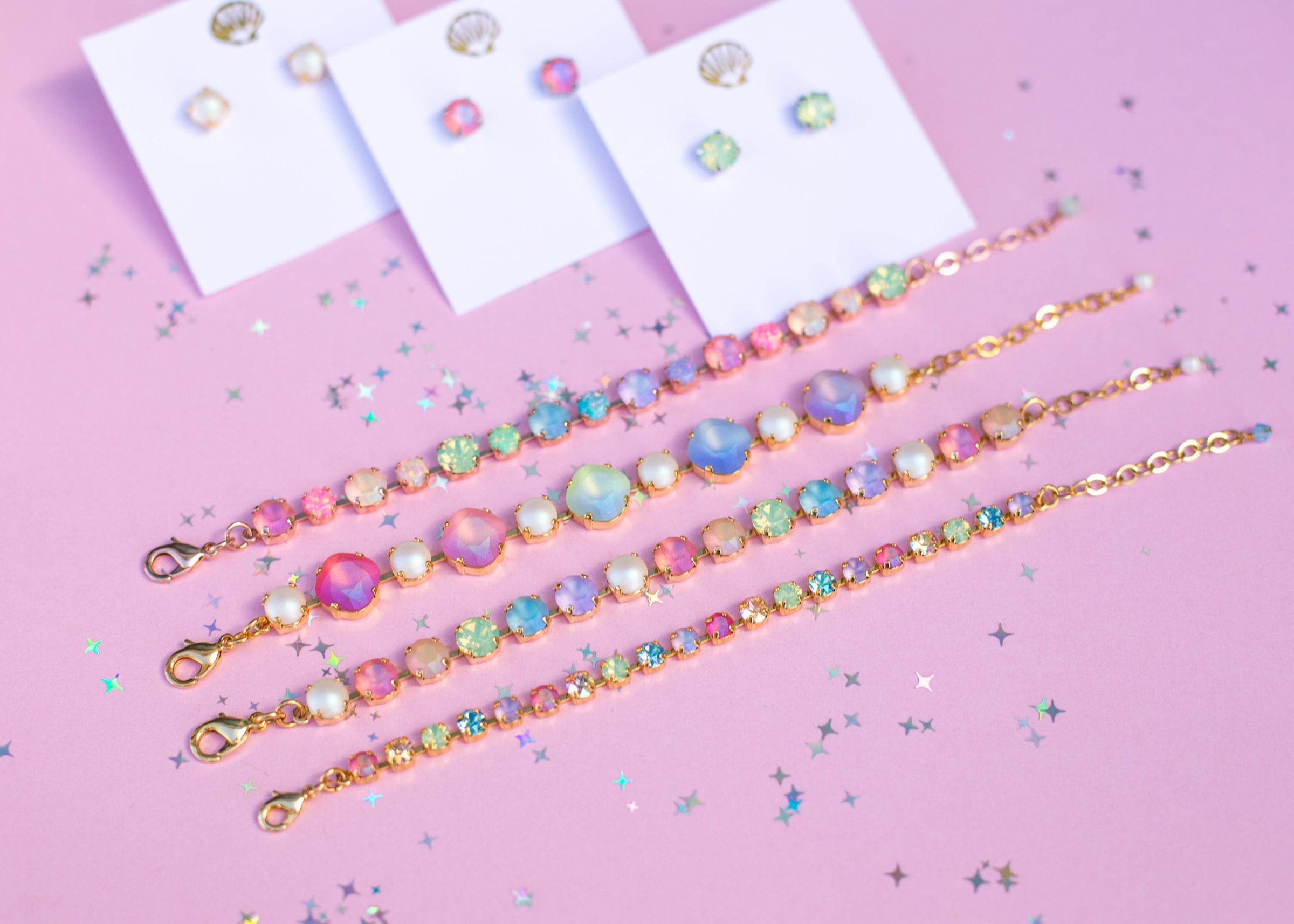 flat lay photo with pink background. 3 pairs of colorful stud earrings. 4 bracelets in pastel rainbows.