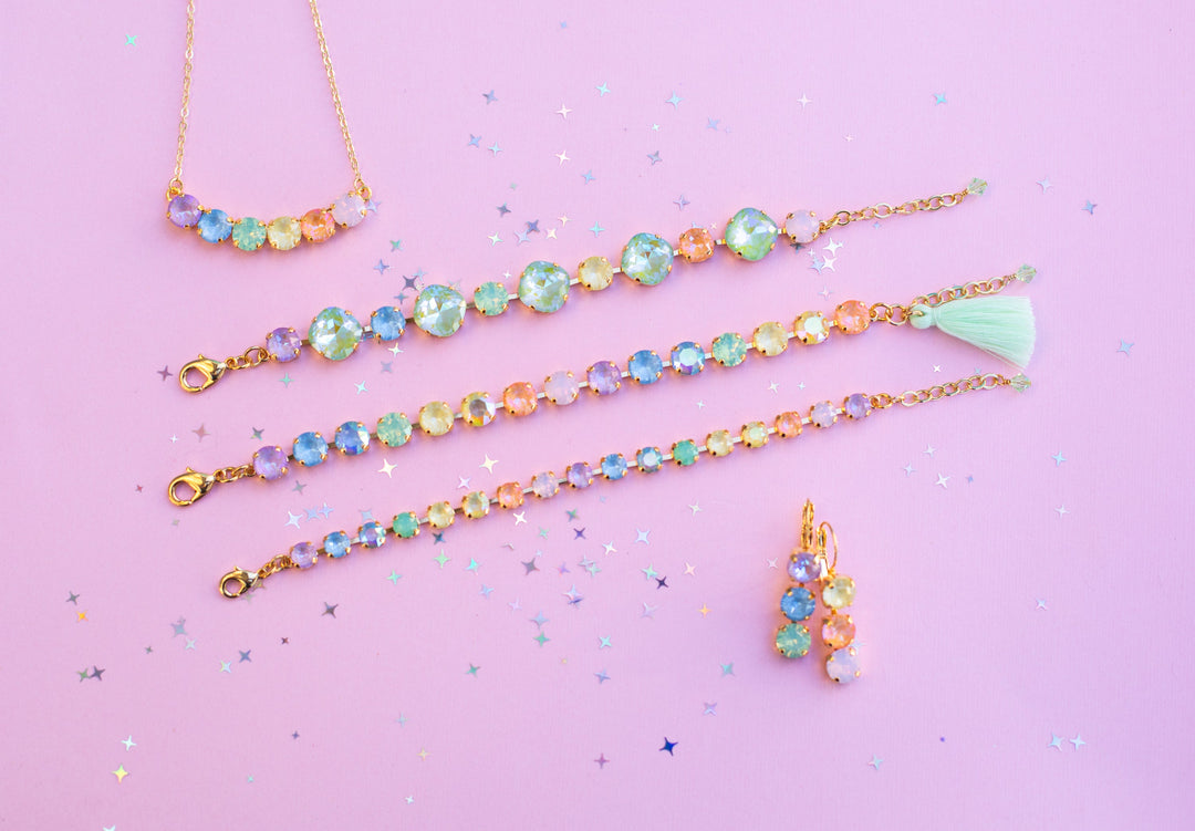 dreamy pastel jewelry pieces. 3 bracelets, a necklace and a pair of earrings on a light pink background.