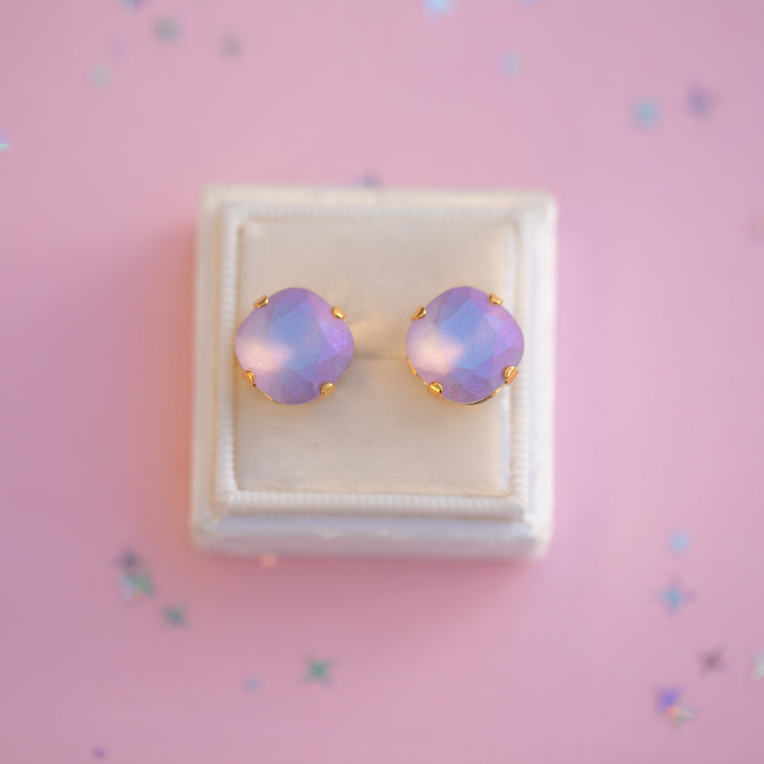 Pair of purple opal stud earrings in a white box on a pink background