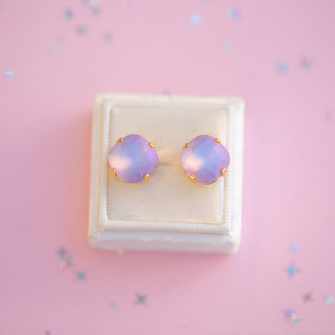 Pair of purple square-shaped earrings in a white box on a pink background
