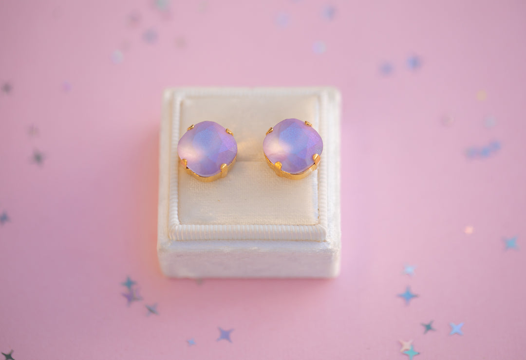 Pair of purple opal earrings in a white box on a pink background with star-shaped decorations.