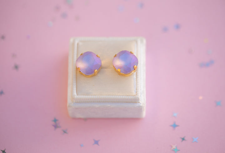 Pair of purple opal earrings in a white box on a pink background with star-shaped decorations.