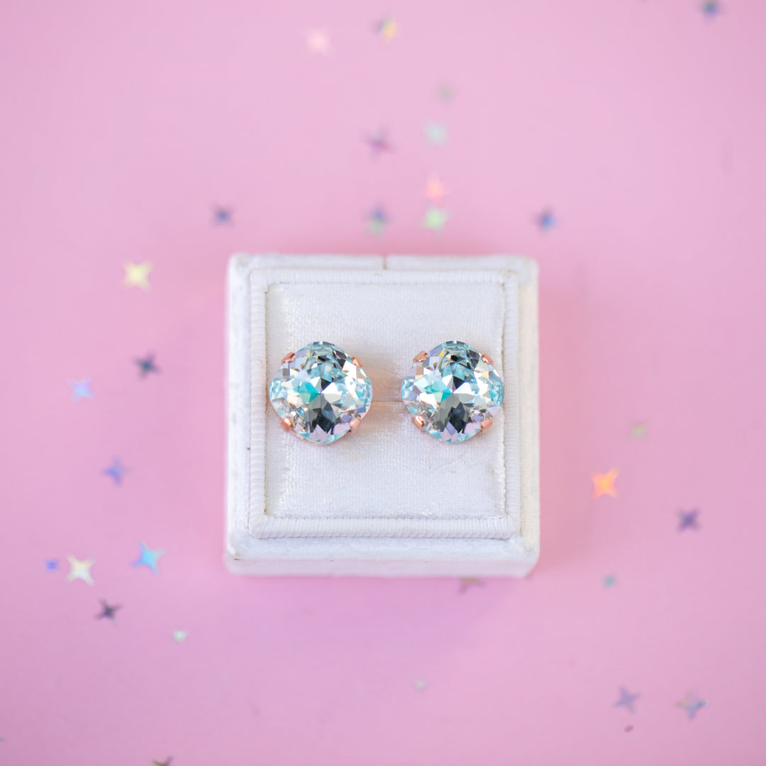 Pair of gemstone stud earrings in a white box on a pink background with star-shaped confetti.
