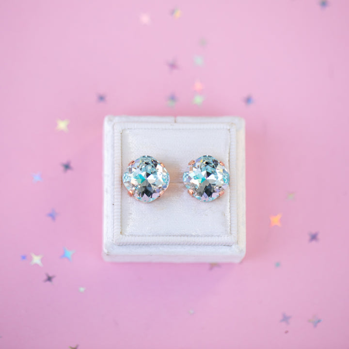 Pair of gemstone stud earrings in a white box on a pink background with star-shaped confetti.
