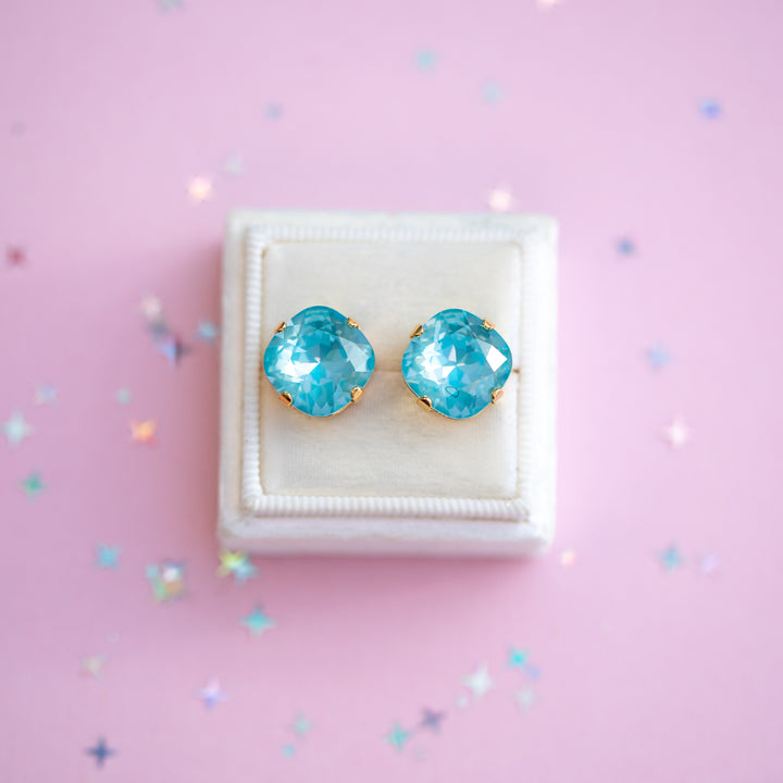 Turquoise earrings on a white cushion against a pink background with confetti