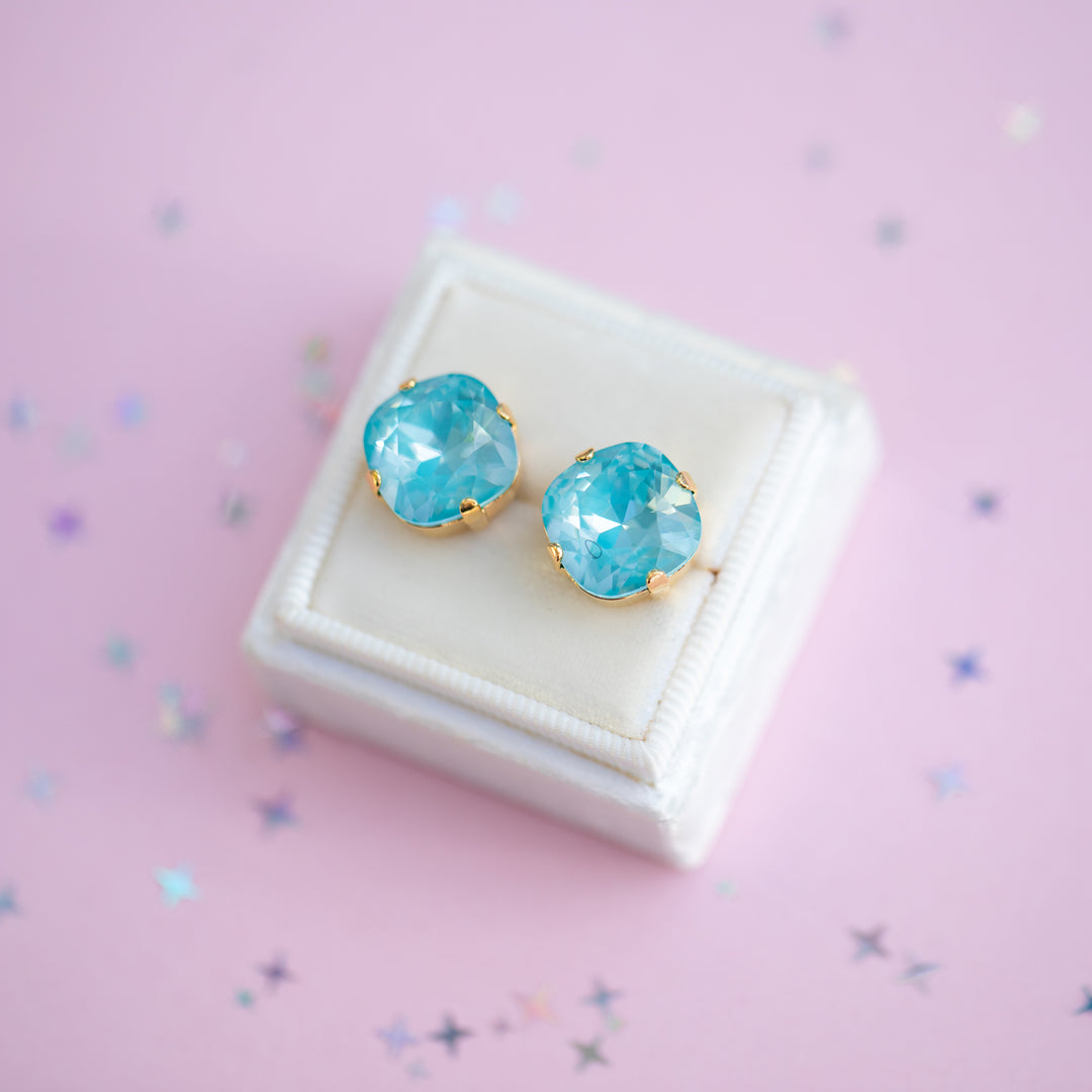 Turquoise earrings with gold accents on a white box against a pink background