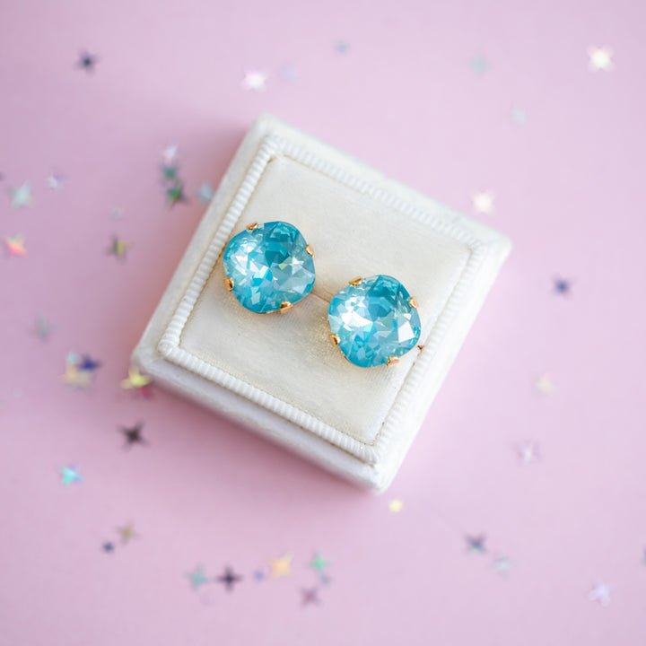 Turquoise earrings on a white cushion with a pink background
