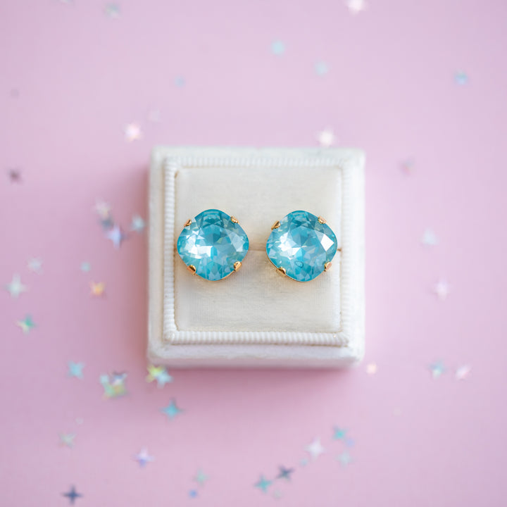 Blue gemstone earrings in a white box on a pink background