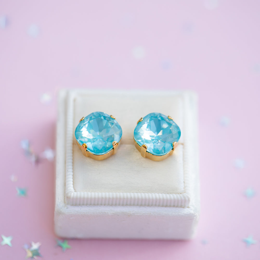 Pair of blue gemstone earrings on a white stand against a pink background