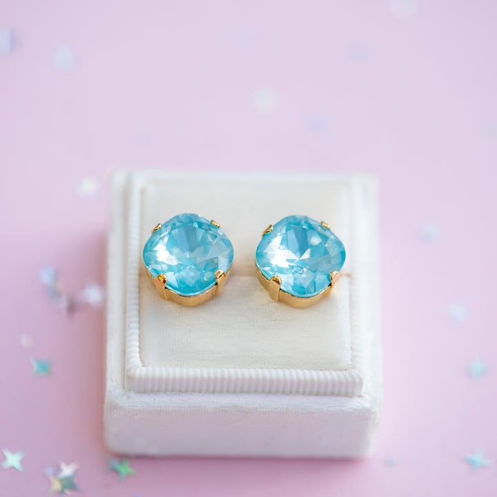 Pair of blue gemstone earrings on a white stand against a pink background