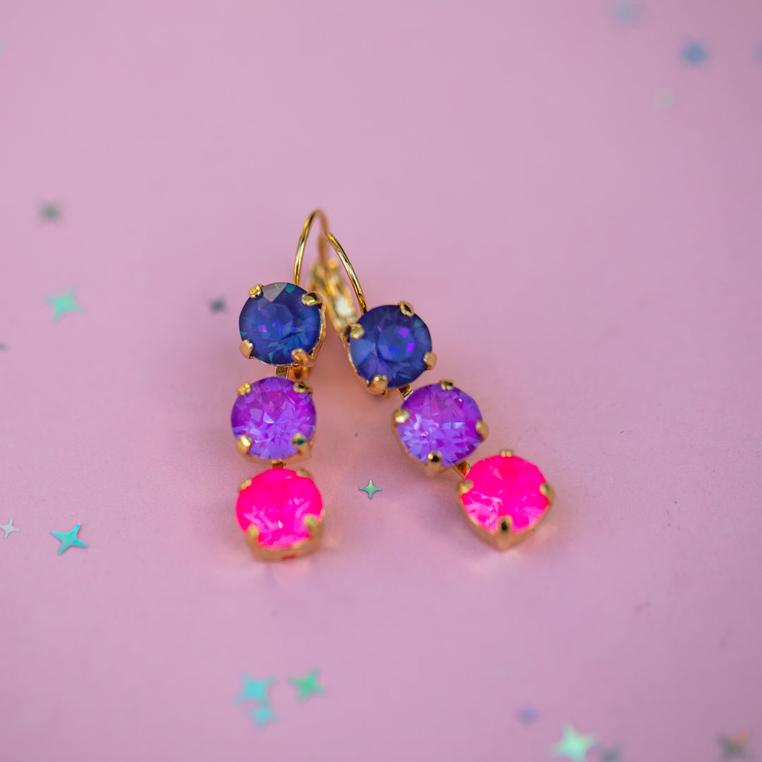 Multicolored gemstone earrings on a pink background with star decorations