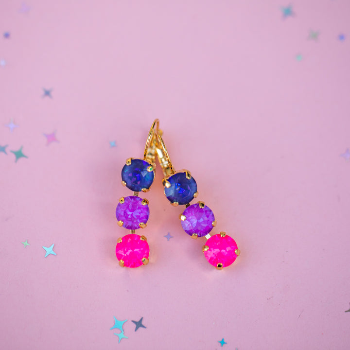 Colorful gemstone earrings on a pink background with star decorations