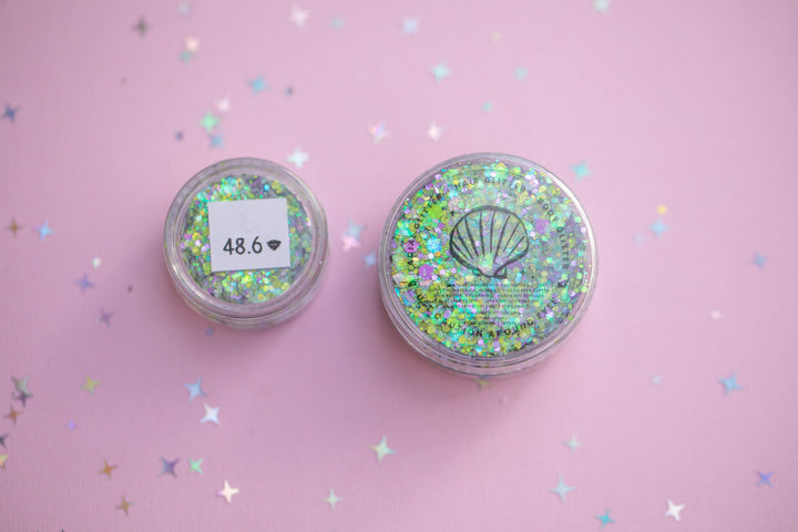 Two small containers of glitter on a pink background with star-shaped confetti.