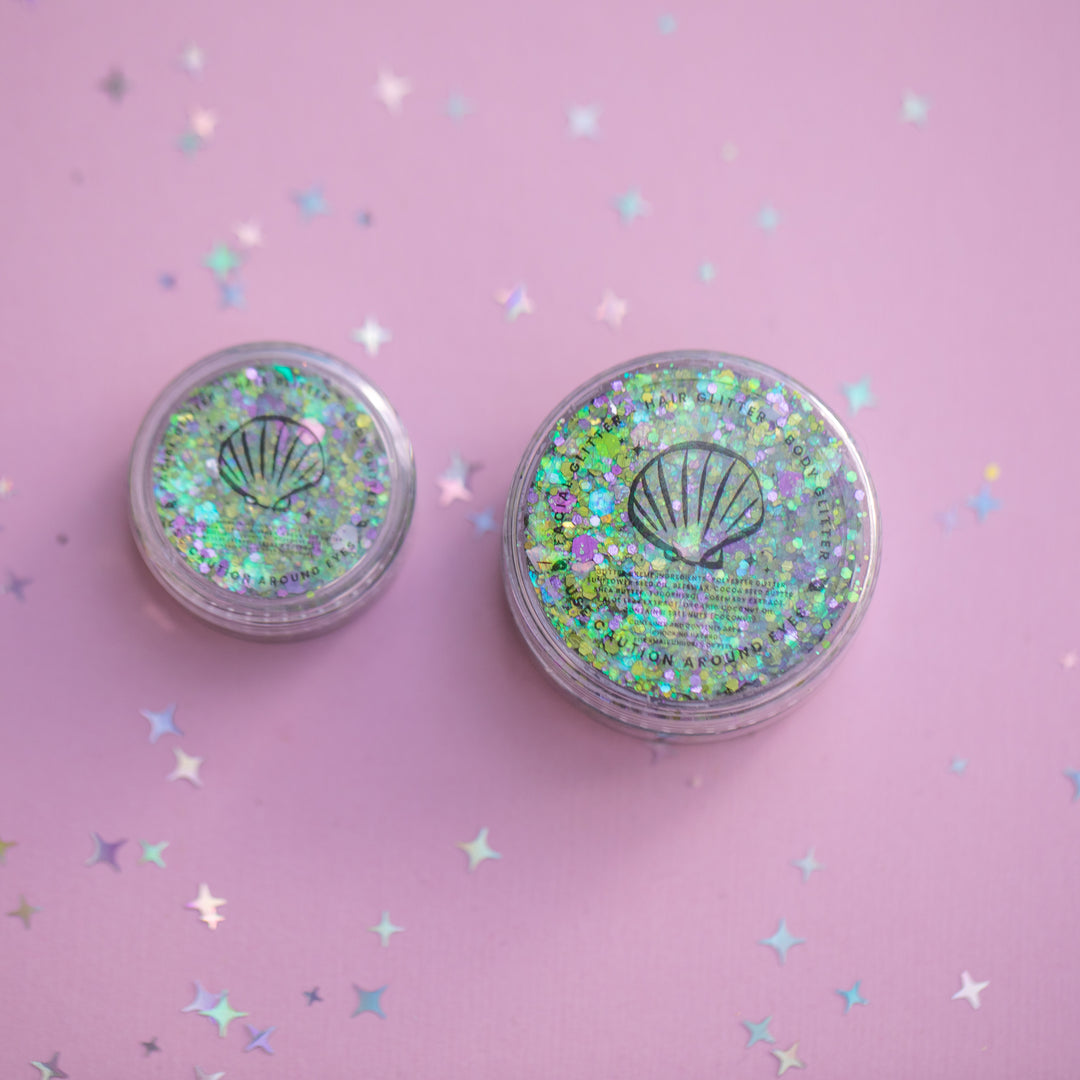 Two small round containers with glittery lids on a pink background with star-shaped confetti.