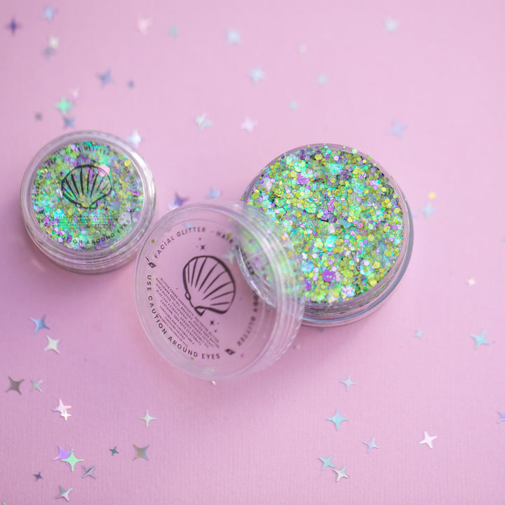 Two containers of glitter on a pink background with star-shaped confetti.