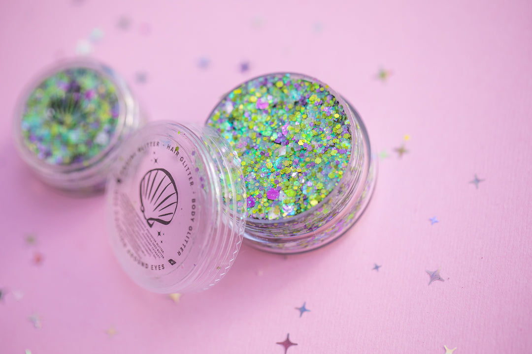 Two containers of glitter on a pink background with star-shaped confetti.