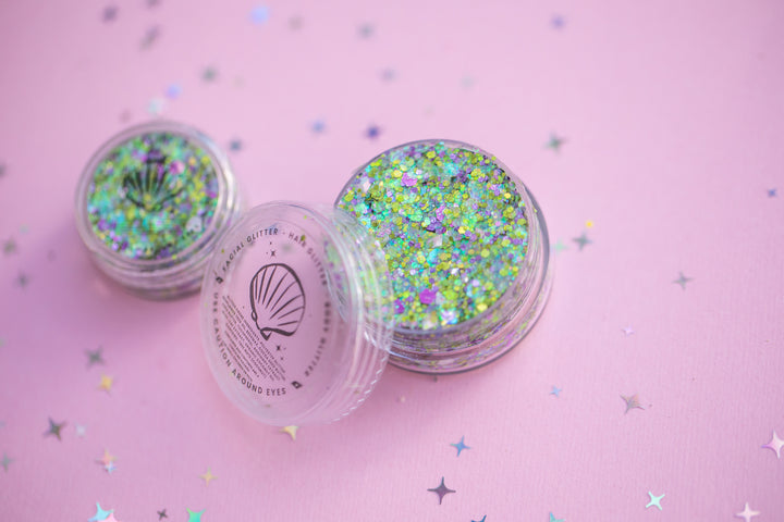 Two containers of glitter on a pink background with star-shaped confetti.