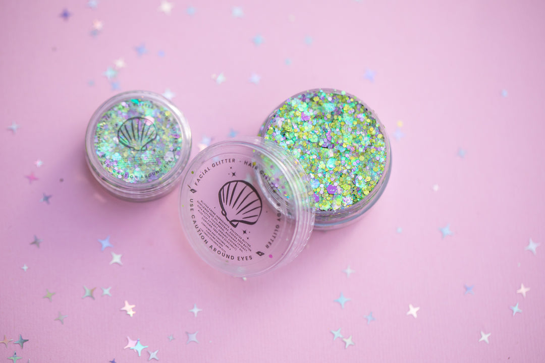 Two containers of glitter with a shell design on a pink background with star-shaped confetti.