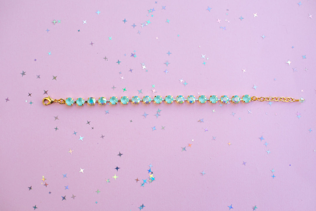 Gold bracelet with green gemstones on a purple background with star confetti