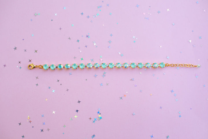 Gold bracelet with green gemstones on a purple background with star confetti