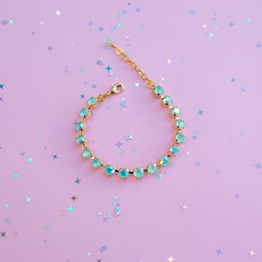 Gold bracelet with turquoise stones on a purple background with star-shaped confetti