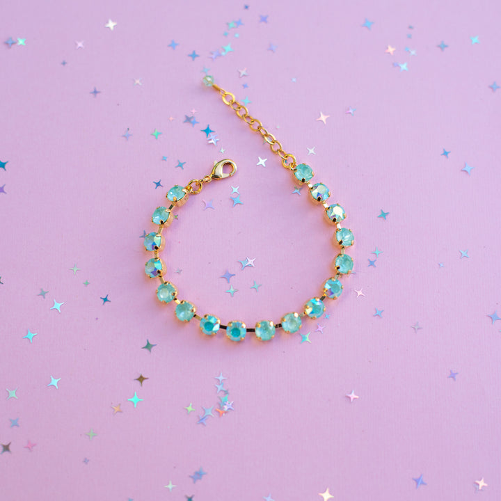 Gold bracelet with turquoise stones on a purple background with star-shaped confetti