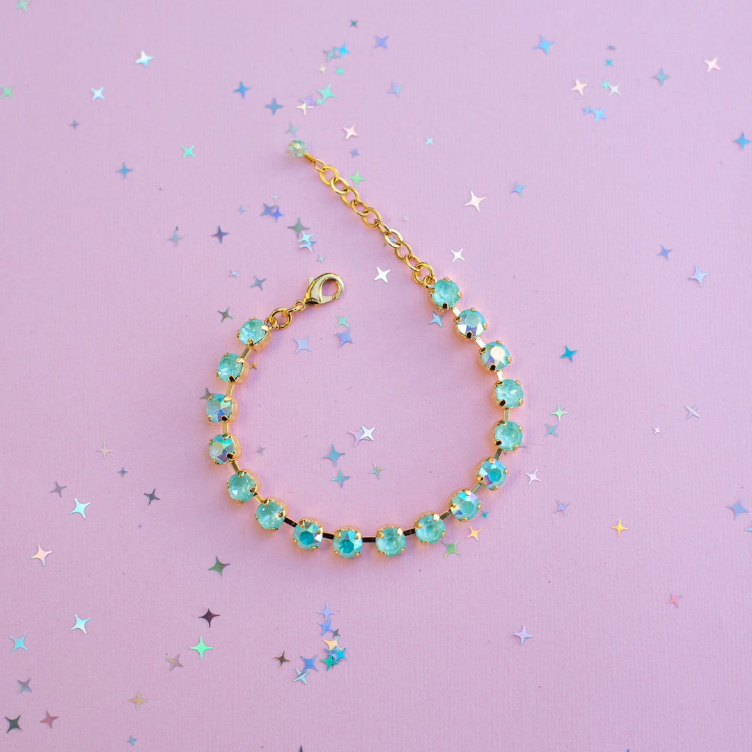 Gold bracelet with turquoise beads on a purple background with star-shaped confetti