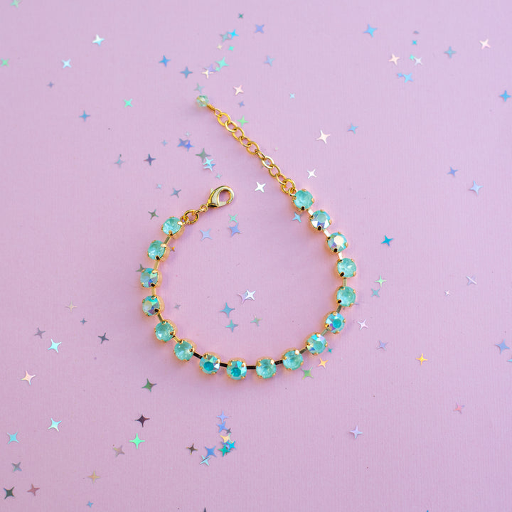 Gold bracelet with turquoise beads on a purple background with star-shaped confetti