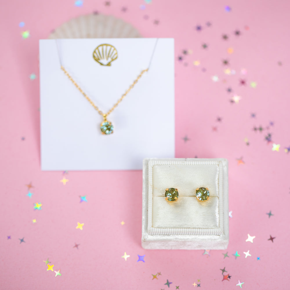 A gold chain necklace with a small olive green crystal pendant on a white card.
