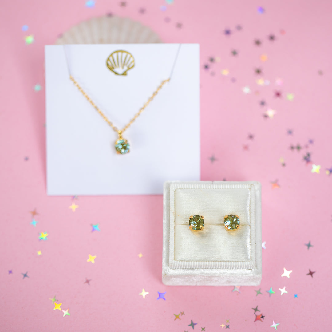 A gold chain necklace with a small olive green crystal pendant on a white card.