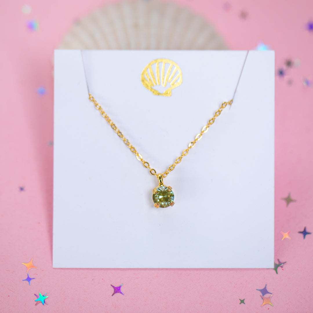 A gold chain necklace with a small olive green crystal pendant on a white card.