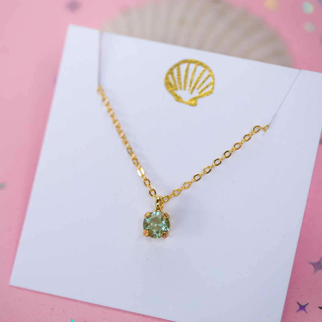 A gold chain necklace with a small olive green crystal pendant on a white card.
