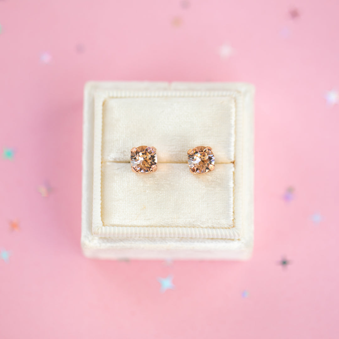 a round pair of Silk crystal studs in a velvet display box on a pink background