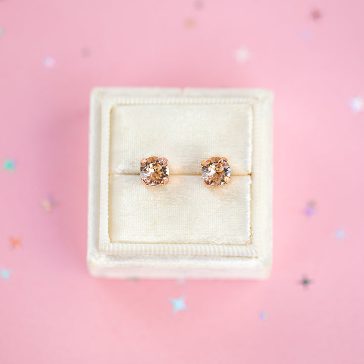 a round pair of Silk crystal studs in a velvet display box on a pink background