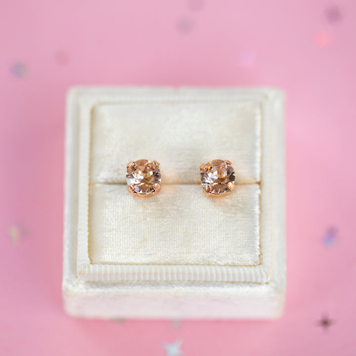  a round pair of Silk crystal studs in a velvet display box on a pink background