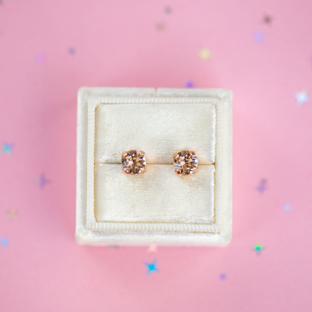 a round pair of Silk crystal studs in a velvet display box on a pink background