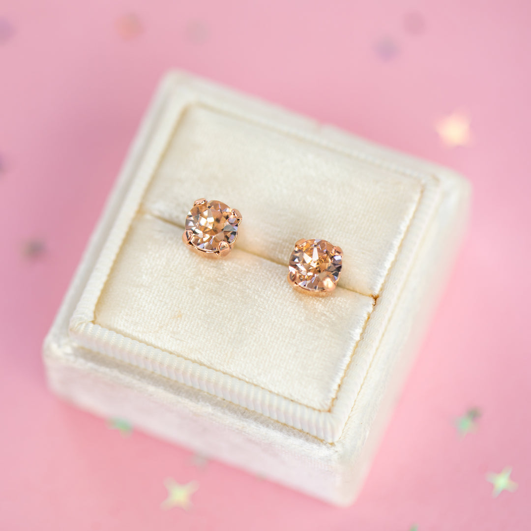 a round pair of Silk crystal studs in a velvet display box on a pink background