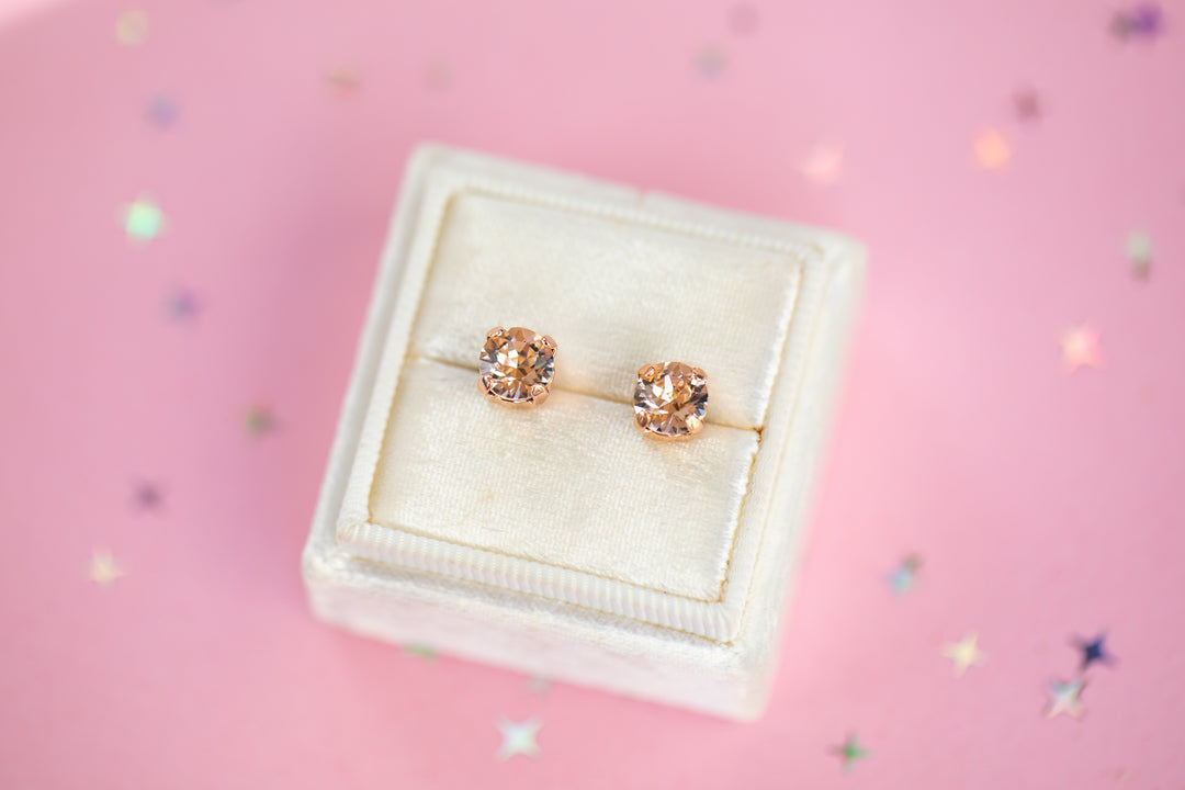 a round pair of Silk crystal studs in a velvet display box on a pink background
