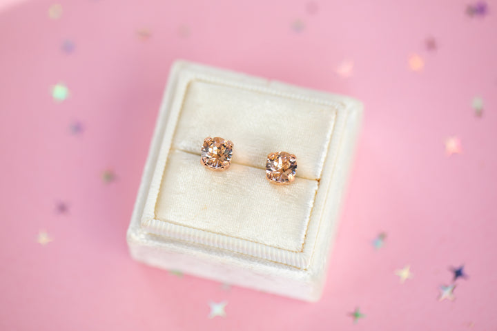 a round pair of Silk crystal studs in a velvet display box on a pink background