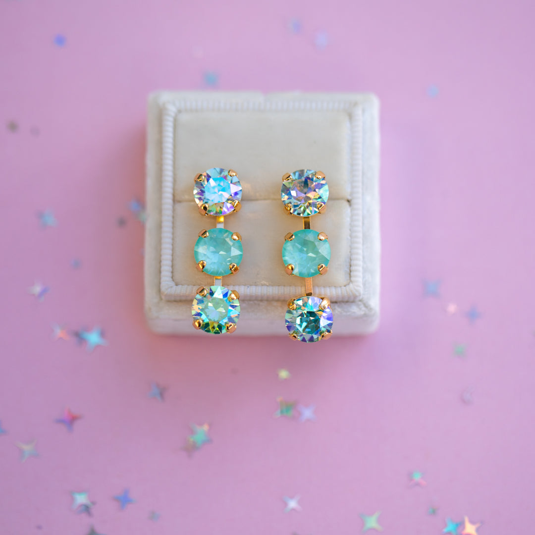 Pair of earrings with turquoise gemstones in a white box on a pink background