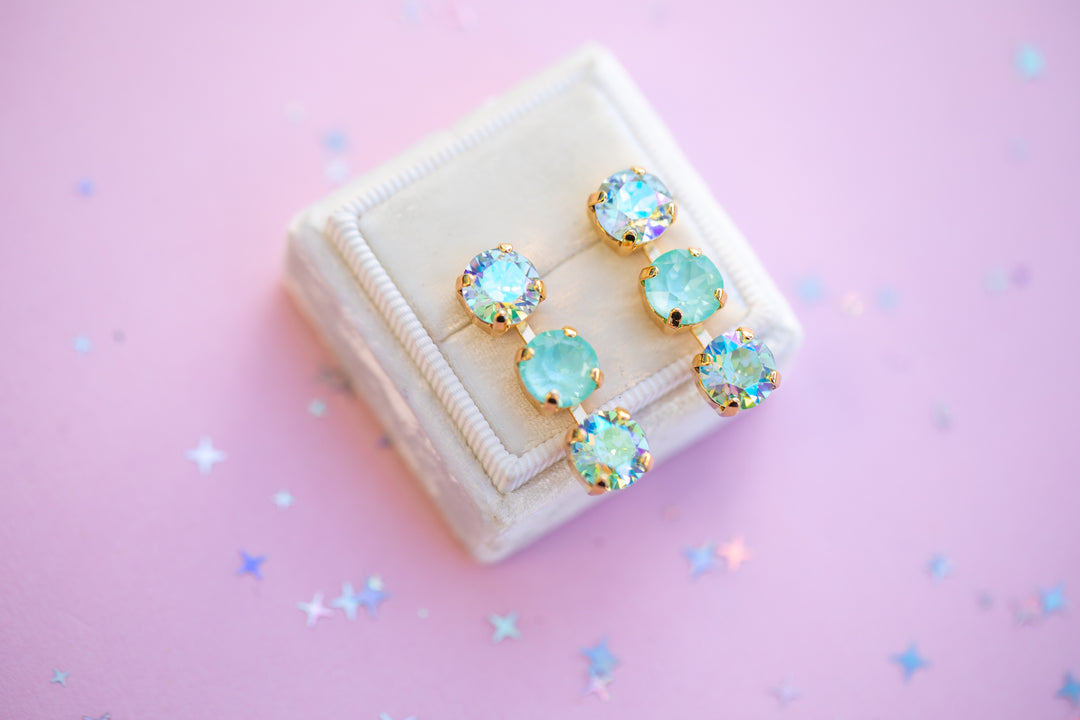 Pair of turquoise earrings on a beige jewelry box with a pink background