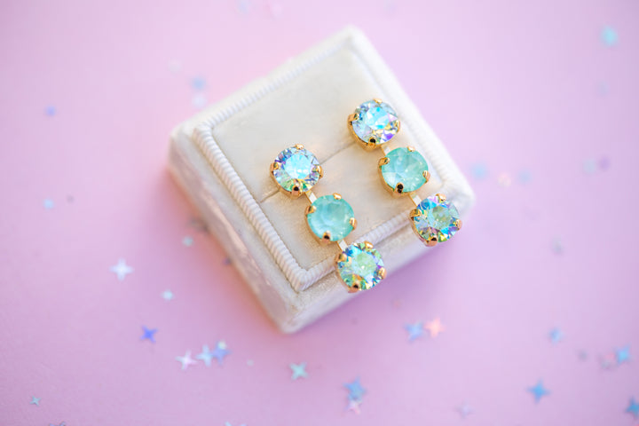 Pair of turquoise earrings on a beige jewelry box with a pink background