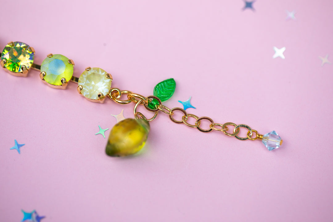 Bracelet with green gemstones and leaf charm on a pink background