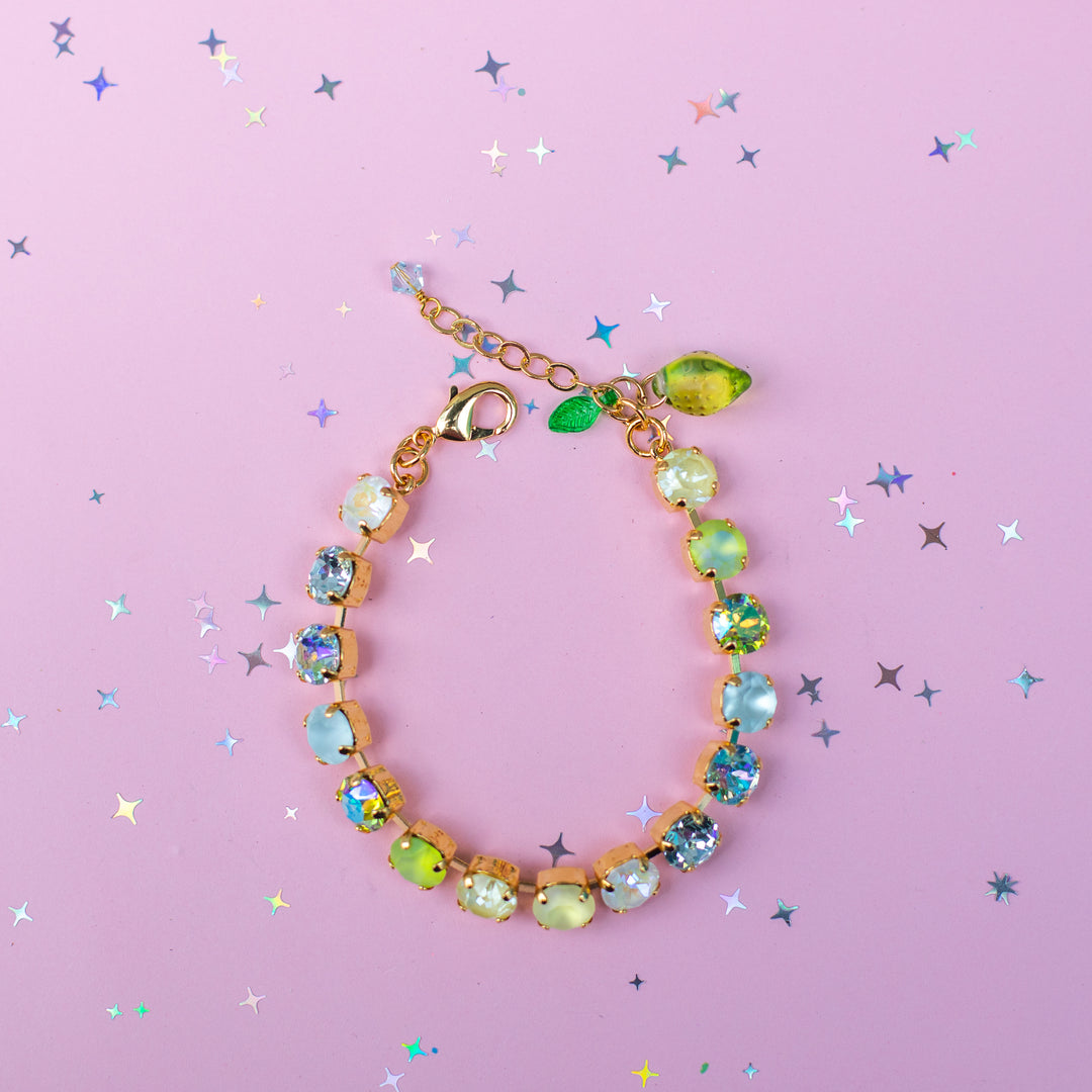 Gold bracelet with colorful gemstones on a pink background with star-shaped confetti