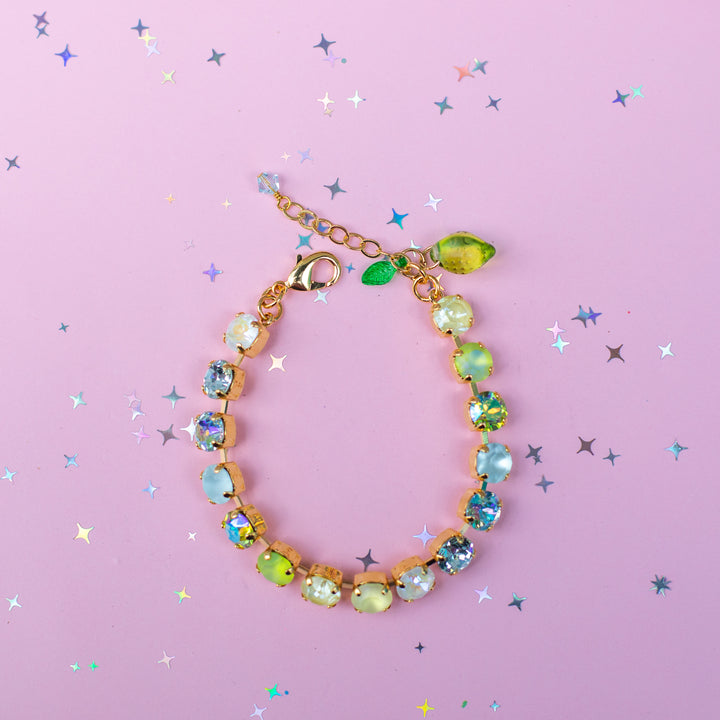 Gold bracelet with colorful gemstones on a pink background with star-shaped confetti