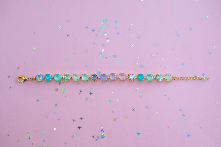 Gold bracelet with colorful gemstones on a pink background