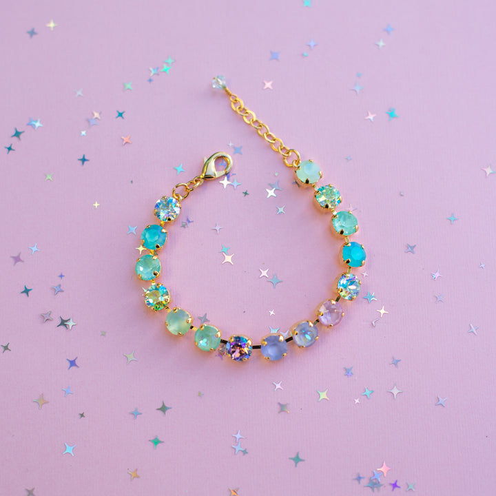 Gold bracelet with colorful beads on a purple background with star-shaped confetti