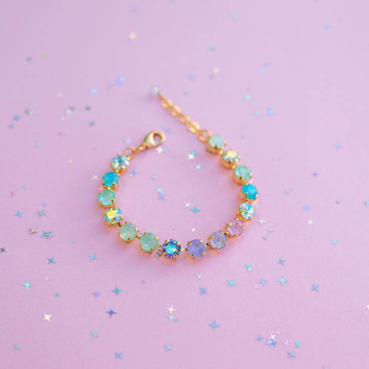 Multicolored crystal bracelet on a pink background with star-shaped confetti