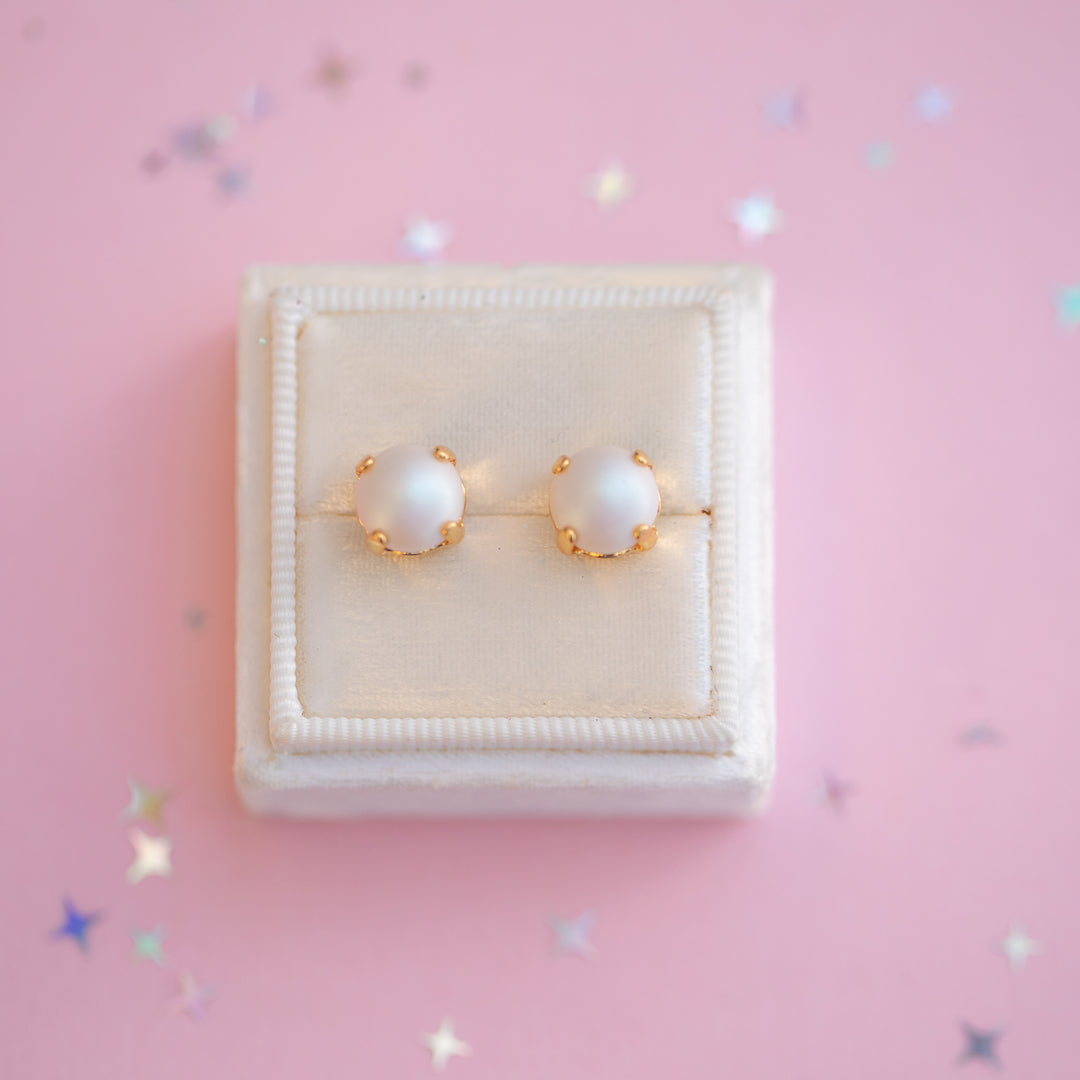 Pearl earrings with gold accents on a pink background